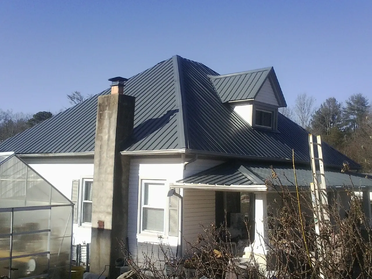 Dark blue standing seam metal roof on a white farmhouse with dormer — Slate & Tile Roof Repair by Roofing Brothers in Glen Campbell