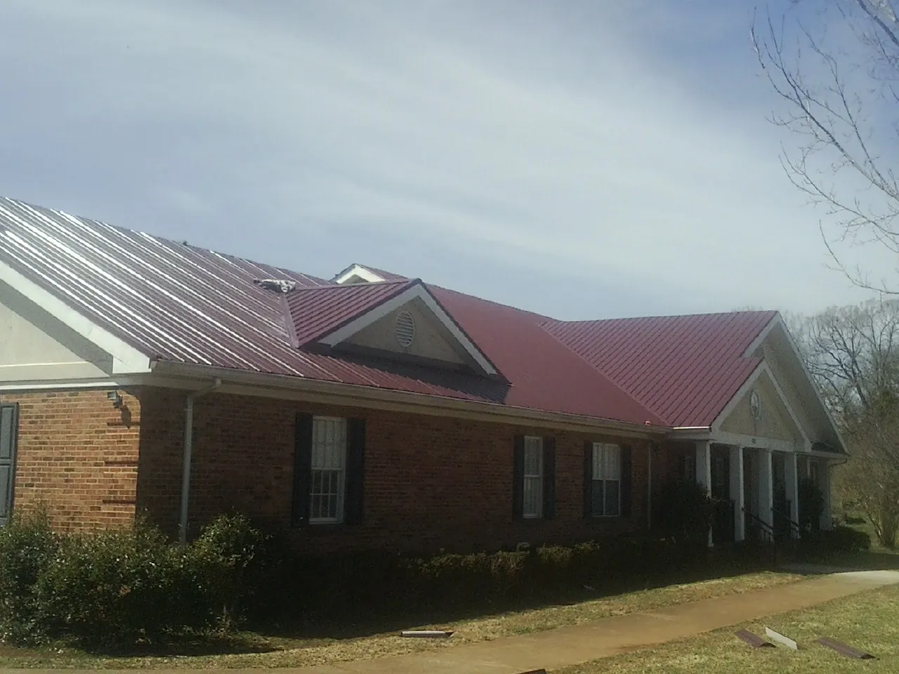 Red metal roof with gabled entries on a long brick building, from a Hail Damage Roof Repair job in Glen Campbell