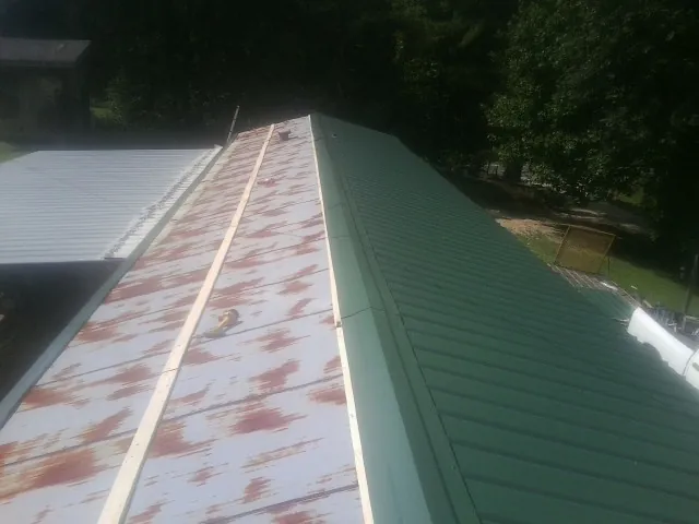 Old rusted panels beside newly installed green metal roofing — Wind Damage Roof Repair by Roofing Brothers in Glen Campbell