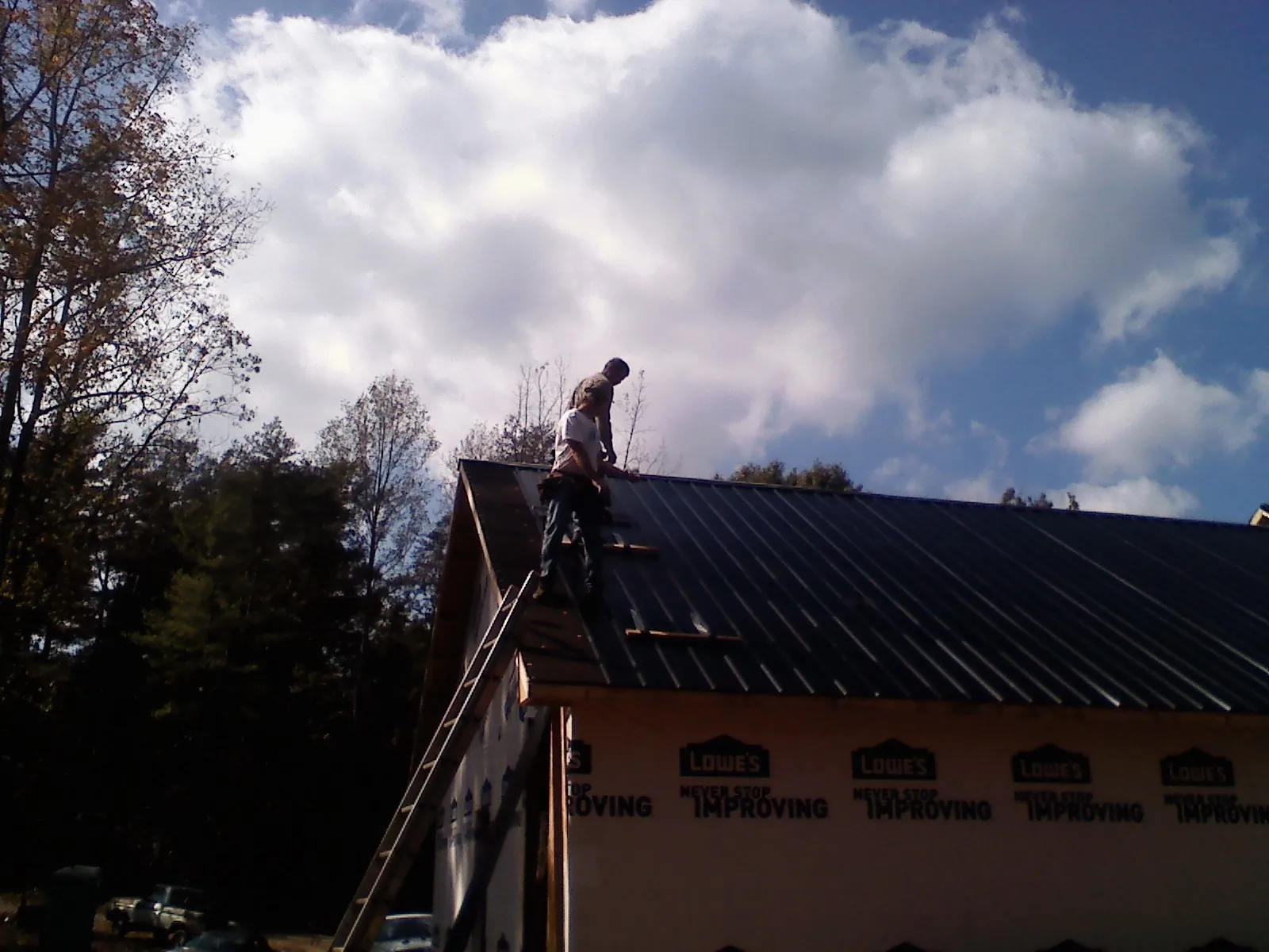Roofer fastening dark metal panels high against a cloudy sky, from a Roof Inspection job in Glen Campbell