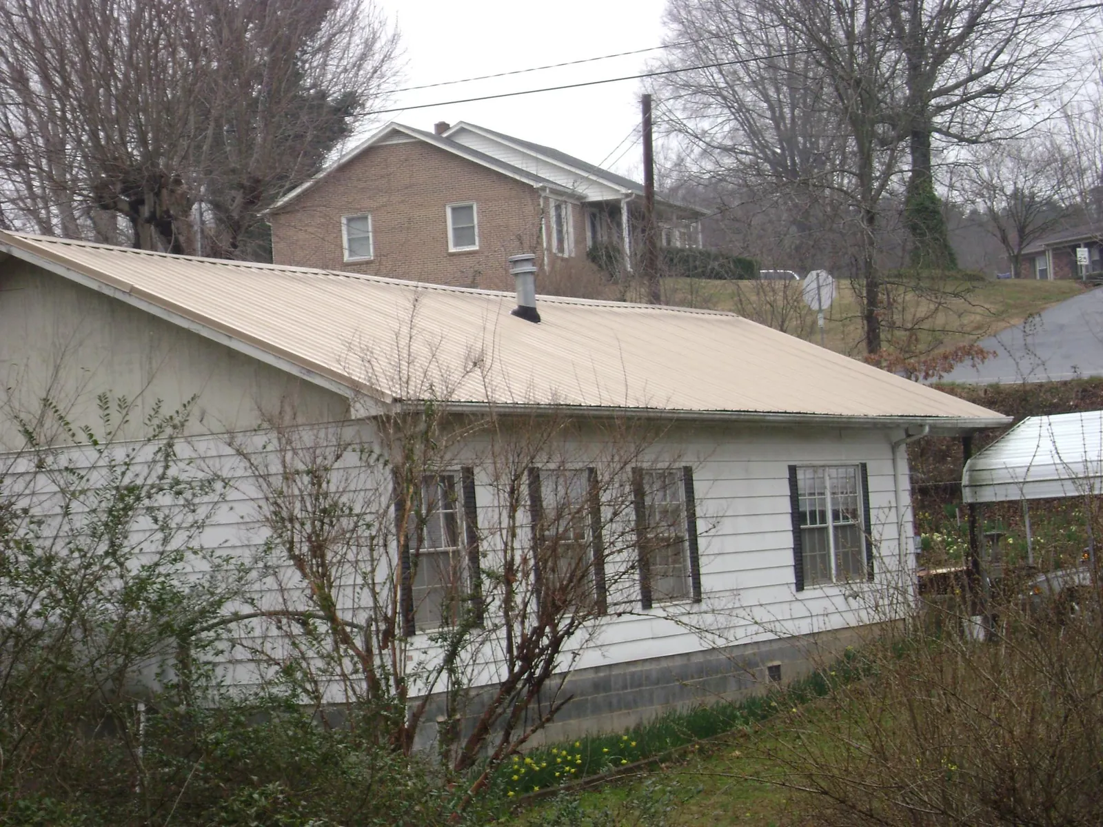 Tan metal roof on a white sided house set into a hillside — Commercial Roofing by Roofing Brothers in Glen Campbell
