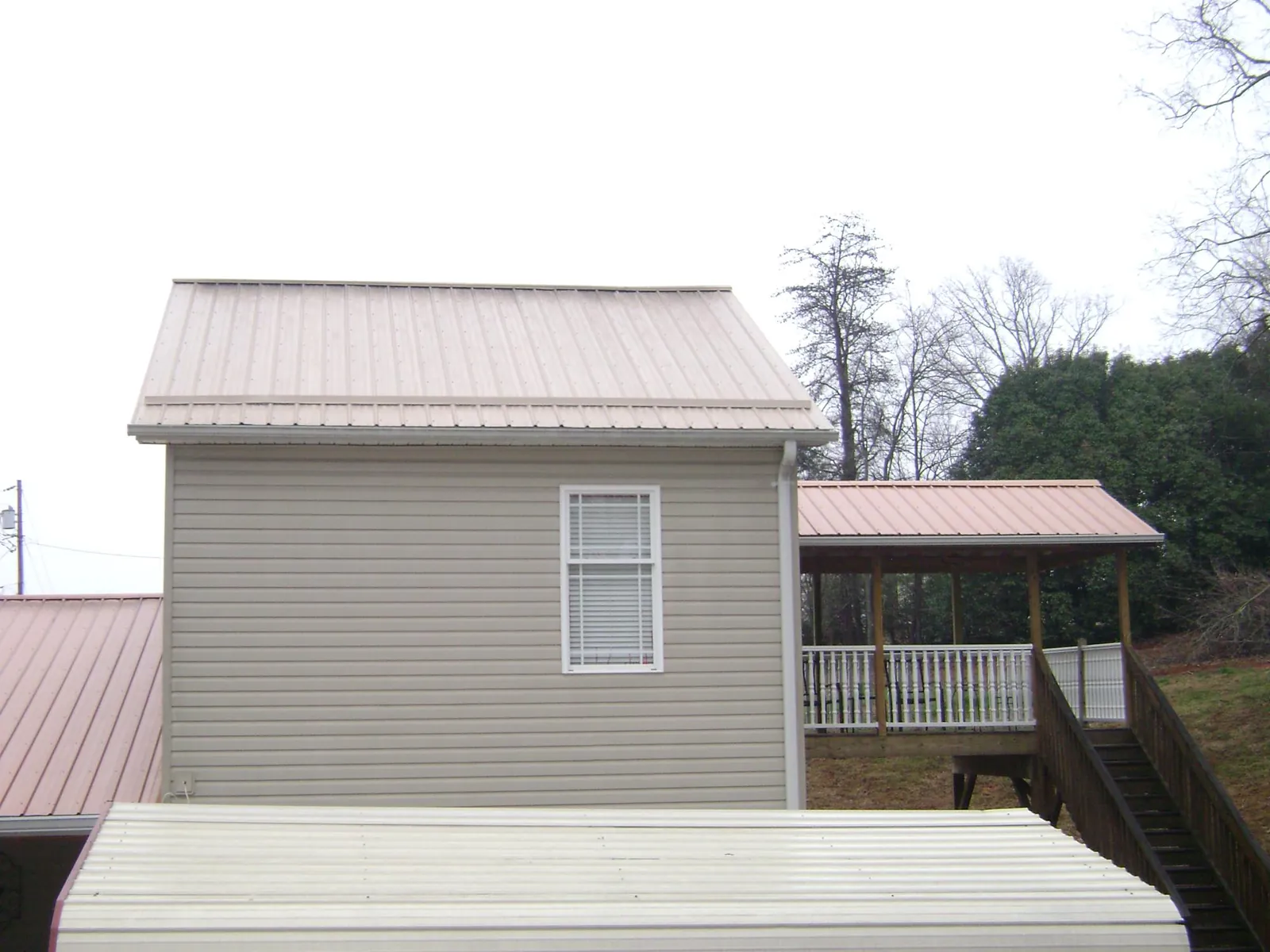 Tan metal roofs on a two story addition and attached porch, from a Roof Replacement job in Glen Campbell